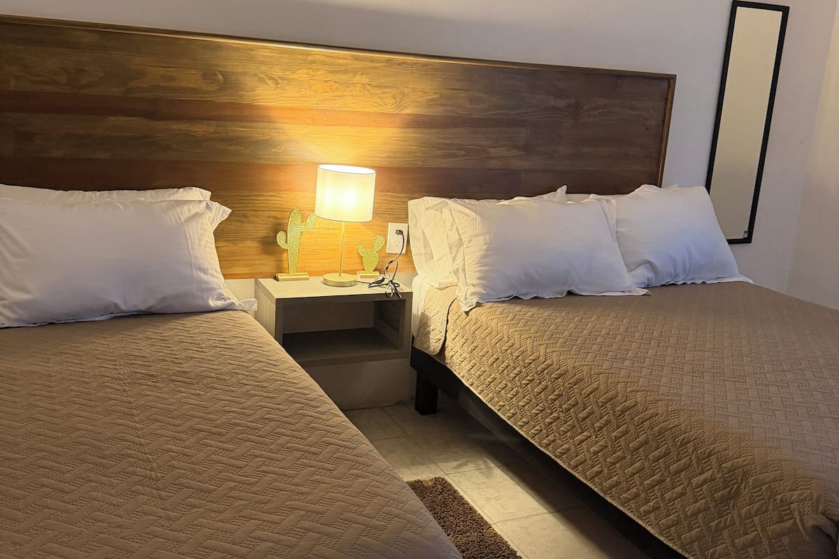 A hotel room with two beds, a wooden headboard, a nightstand with a lamp, and a mirror on the wall.