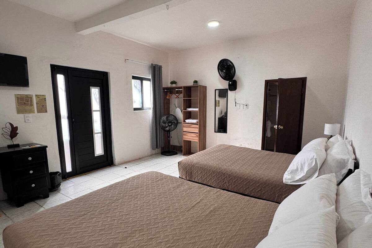 A bedroom with two beds, a wardrobe, a mirror, and a fan.