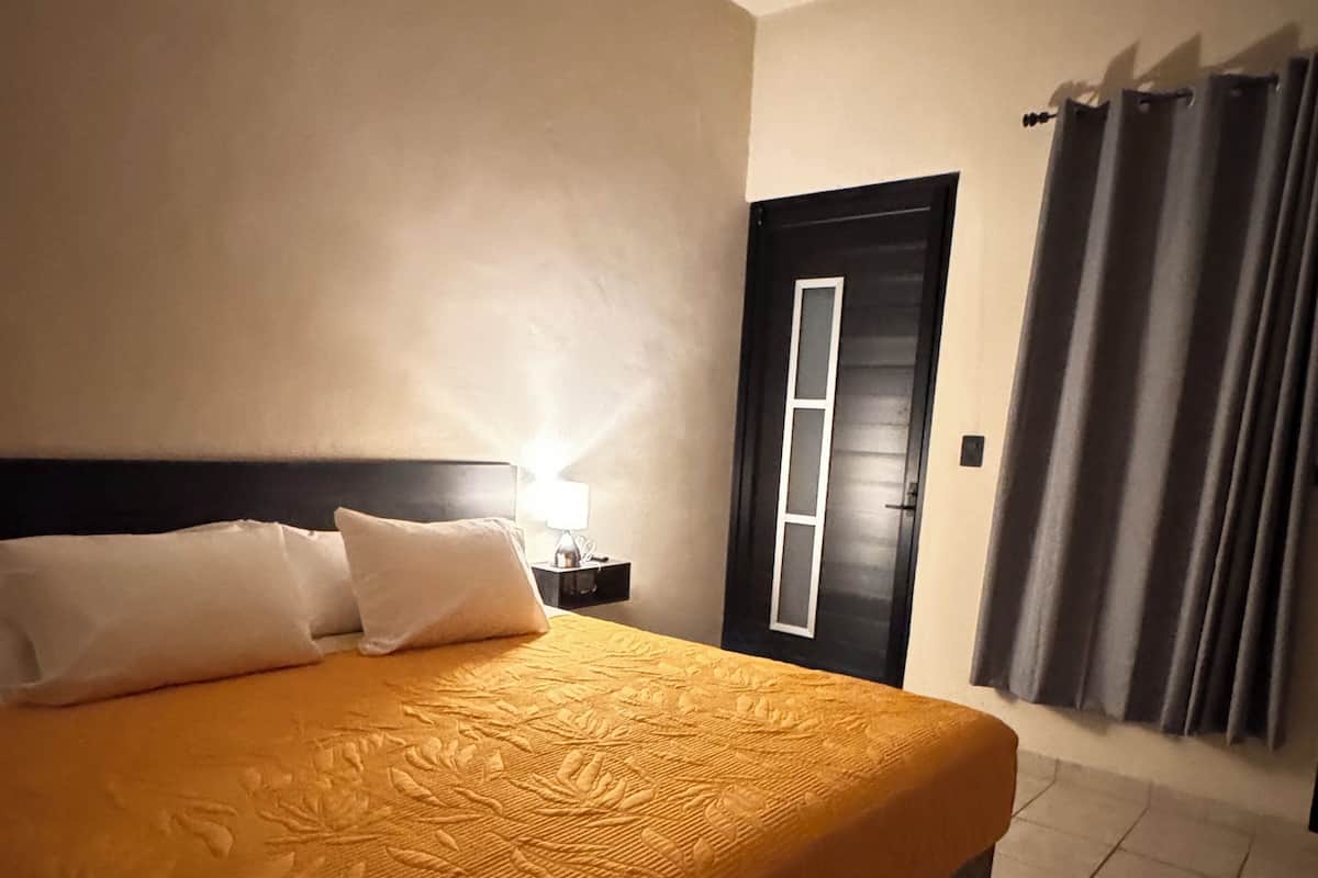 A hotel room with a bed, a nightstand, a lamp, a door, and curtains.
