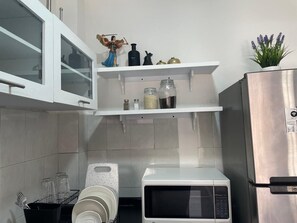 Eine kompakte Küche mit weißen Schränken, einem Edelstahlkühlschrank, einer Mikrowelle und einem kleinen Regal mit Dekoration.