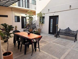 Ein Innenhof mit Tisch und Stühlen, Topfpflanzen, einer Bank und einer Treppe, die zu einer oberen Etage führt.