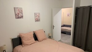 Een slaapkamer met een bed, twee kussens, een nachtkastje met een lamp en twee aan de muur hangende schilderijen.