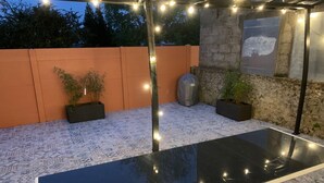 Een terras op het dak met een glazen tafel, potplanten, lichtjes en een stenen muur.