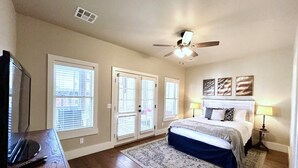 A bedroom with a bed, a ceiling fan, a TV, and a window with blinds.