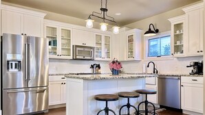 A modern kitchen with white cabinetry, stainless steel appliances, and a central island with stools.