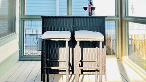 A covered patio with two wicker chairs and a table, overlooking a blue house.