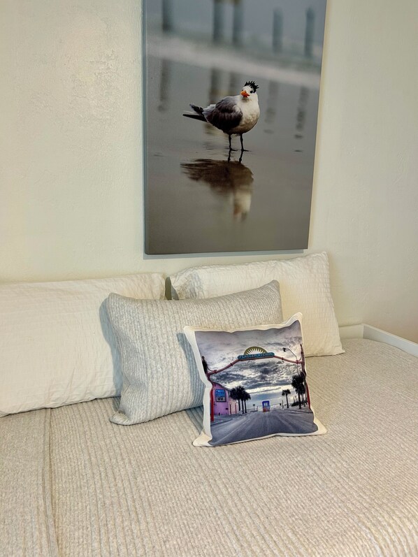 A bedroom with a bed, pillows, and a wall-mounted picture of a bird.