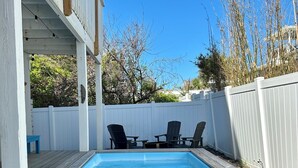 En trädgård med en pool, ett trädäck och två Adirondack-stolar.