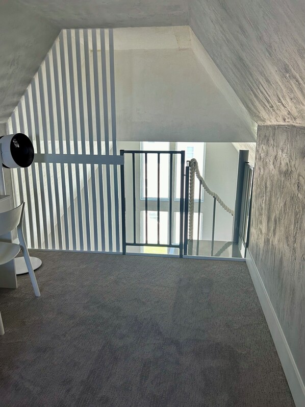 Una habitación con techo inclinado, una silla blanca, una lámpara y vistas al exterior.