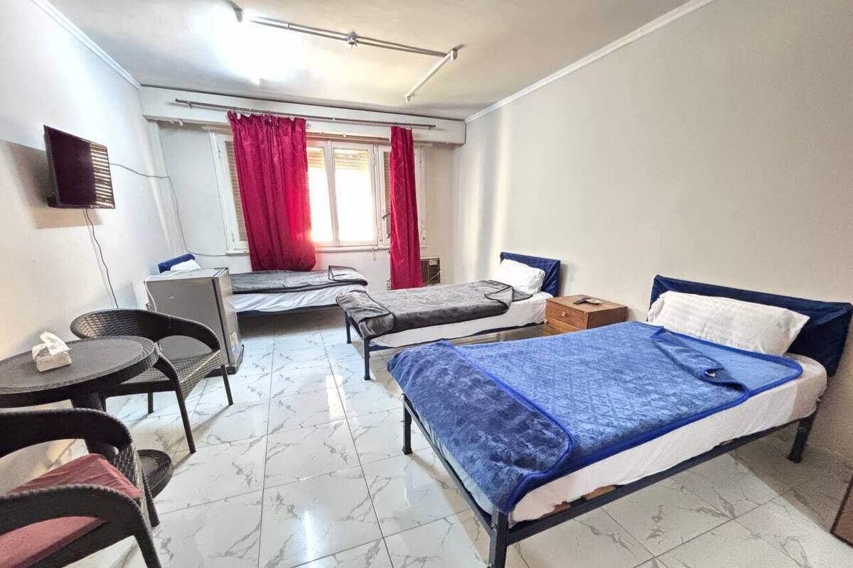 A hotel room with a bed, a desk, a chair, a small table, and a window with curtains.