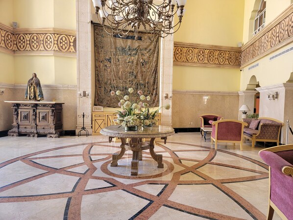 A lobby with a marble floor, a round table with a floral centerpiece, a statue on a pedestal, and ornate wall decorations.