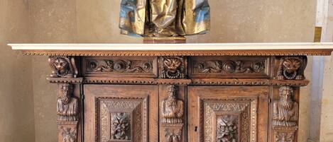 Una estatua de una figura vestida sobre un altar de madera con tallas intrincadas y una base de mármol.