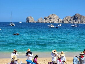 A beach with people, boats, and rocky cliffs in the background.