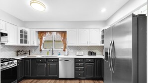 Una cocina moderna con armarios blancos, un refrigerador de acero inoxidable, un lavavajillas y piso de madera.