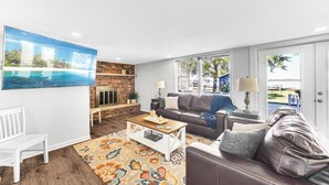 Una sala de estar con chimenea, un televisor grande, un sofá, una mesa de centro y vistas al exterior.