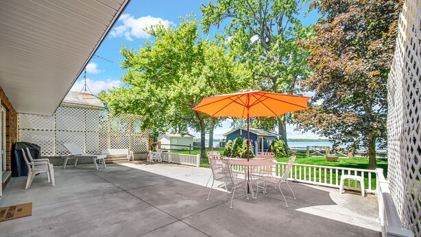 Un patio techado con una mesa y sillas, una sombrilla naranja y vistas a un lago.