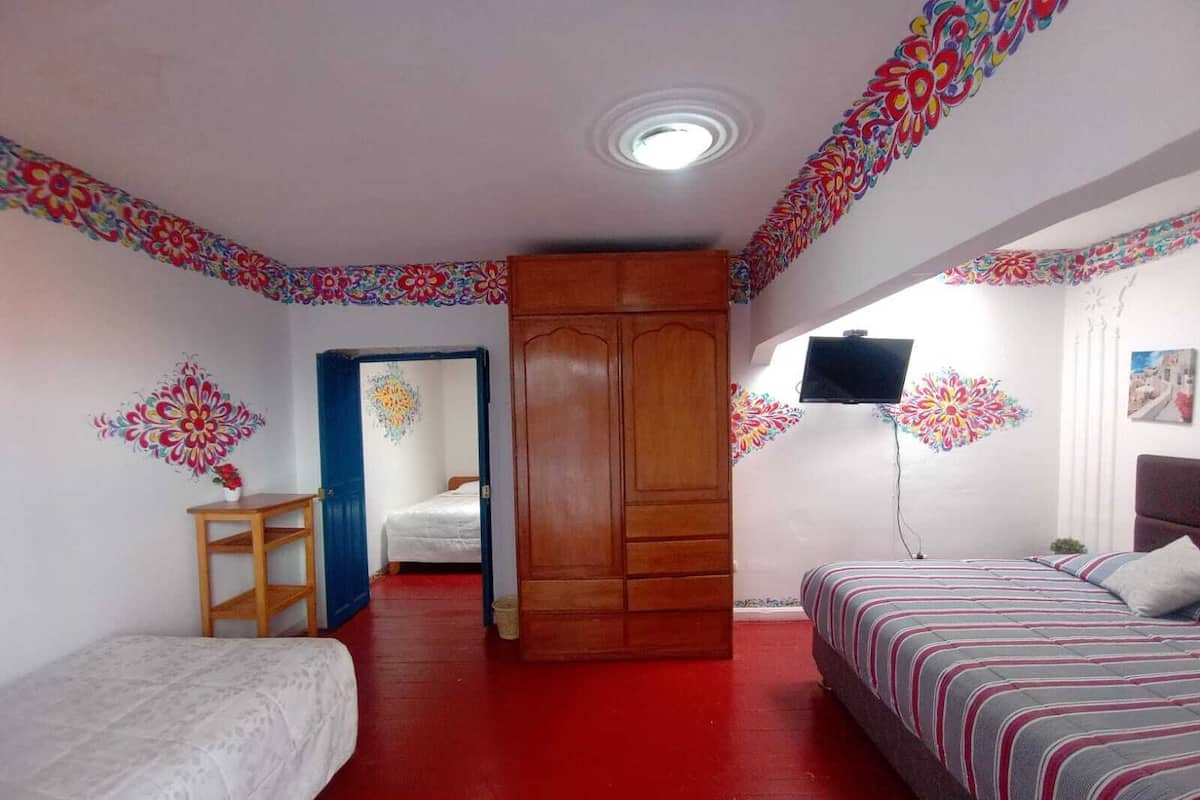 A room with two beds, a wardrobe, a television, and colorful wall decorations.