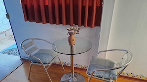 A small room with a glass table and two chairs, a red curtain, and a small vase with dried flowers. - munay apartment (Cusco)