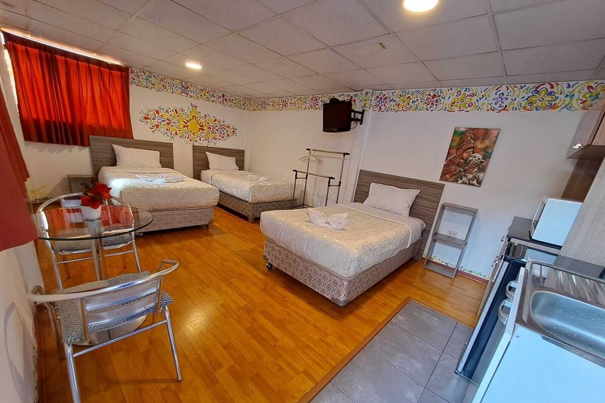 A hotel room with two beds, a small kitchenette, a dining table, and a chair.