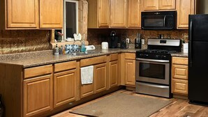 Une cuisine avec des meubles de rangement en bois, une cuisinière en acier inoxydable, un four à micro-ondes et un réfrigérateur noir.