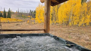 Un bain à remous avec de l’eau en mouvement, situé devant un paysage d’arbres aux couleurs automnales et une zone boisée.