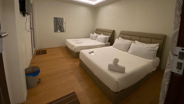 A hotel room with two beds, a small bedside table, a wall-mounted TV, and a ceiling light fixture. - Le Deon Hotel (Batu Gajah)
