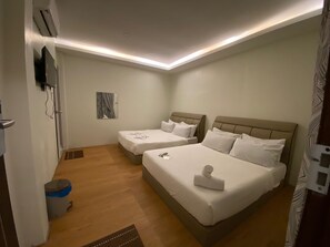 A hotel room with two beds, a small bedside table, a wall-mounted TV, and a ceiling light fixture. - Le Deon Hotel (Batu Gajah)