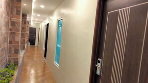 A hallway with wooden flooring, a stone wall on one side, and a door with a vertical stripe pattern. - Le Deon Hotel (Batu Gajah)
