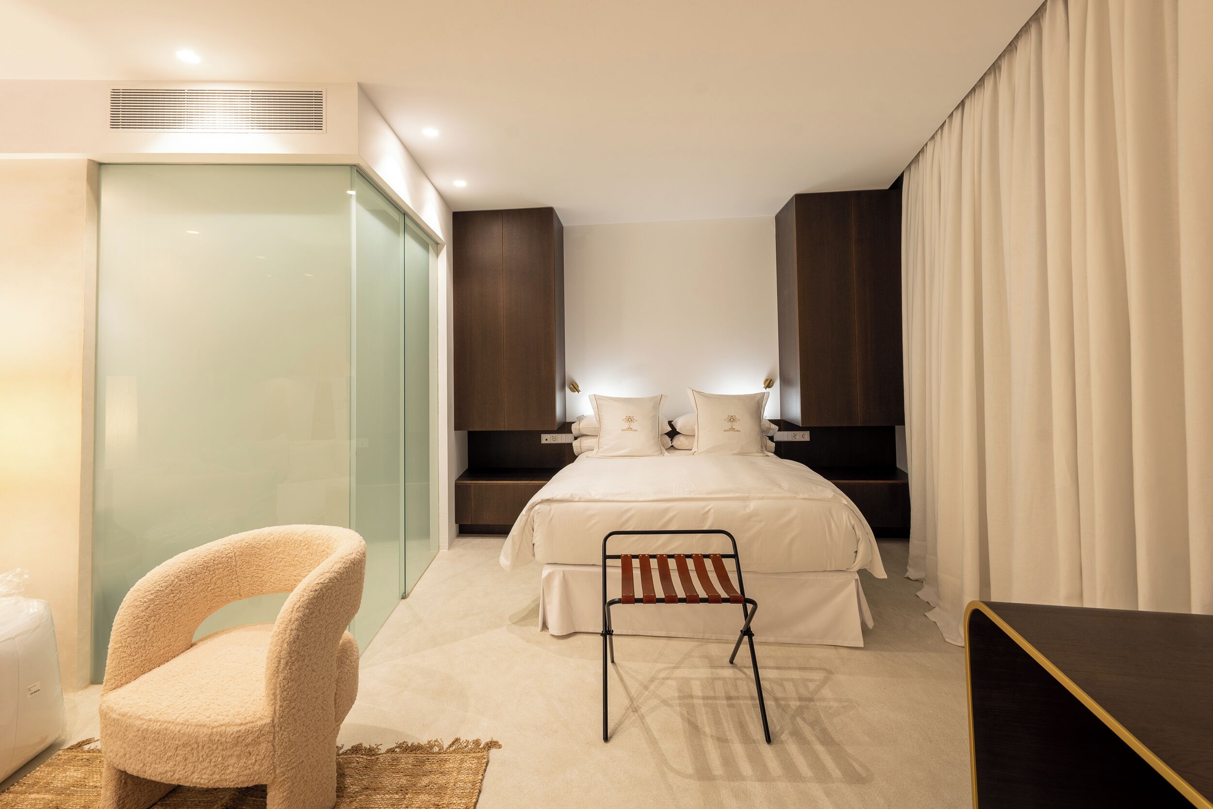 Una habitación de hotel moderna con una cama, una silla, una mesita de noche y un armario.