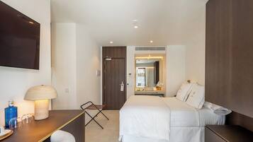 A modern hotel room with a large bed, a desk with a lamp, a flat-screen TV, and a small seating area.