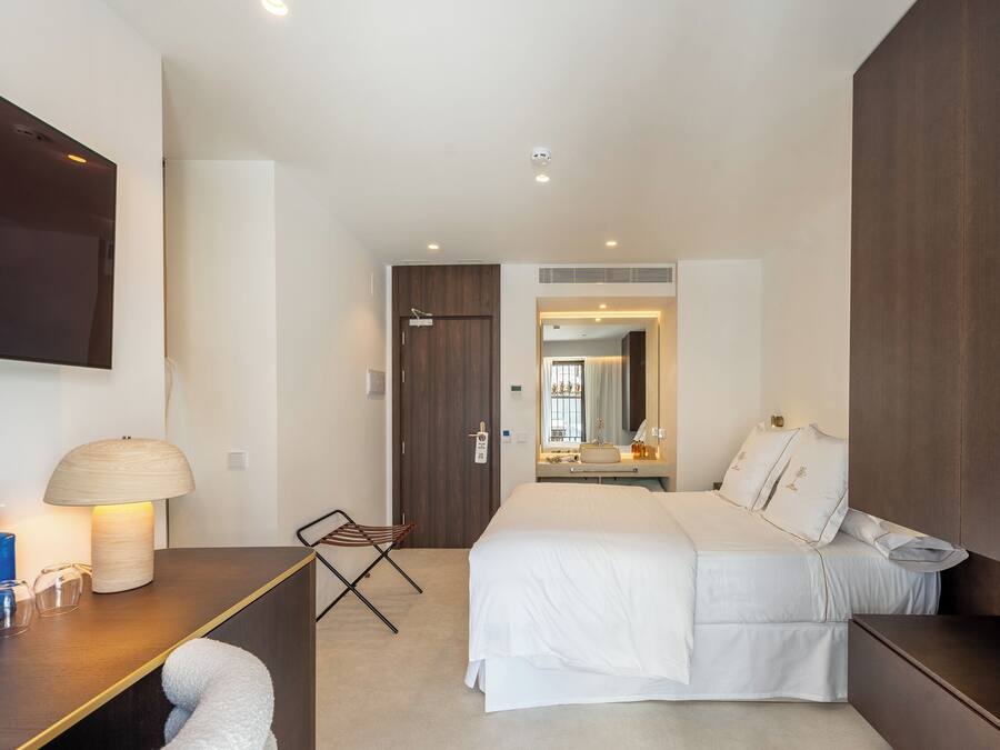 A modern hotel room with a large bed, a desk with a lamp, a flat-screen TV, and a small seating area.