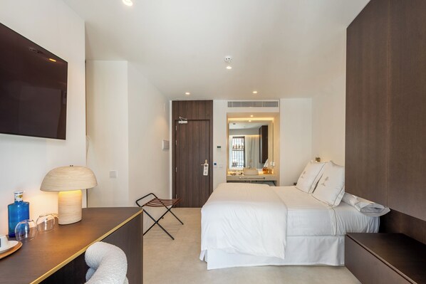 A modern hotel room with a large bed, a desk with a lamp, a flat-screen TV, and a small seating area.