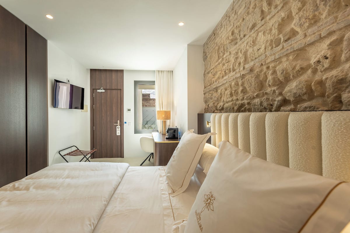 Une chambre d’hôtel avec un grand lit, un bureau, une chaise et un mur à la texture de pierre.