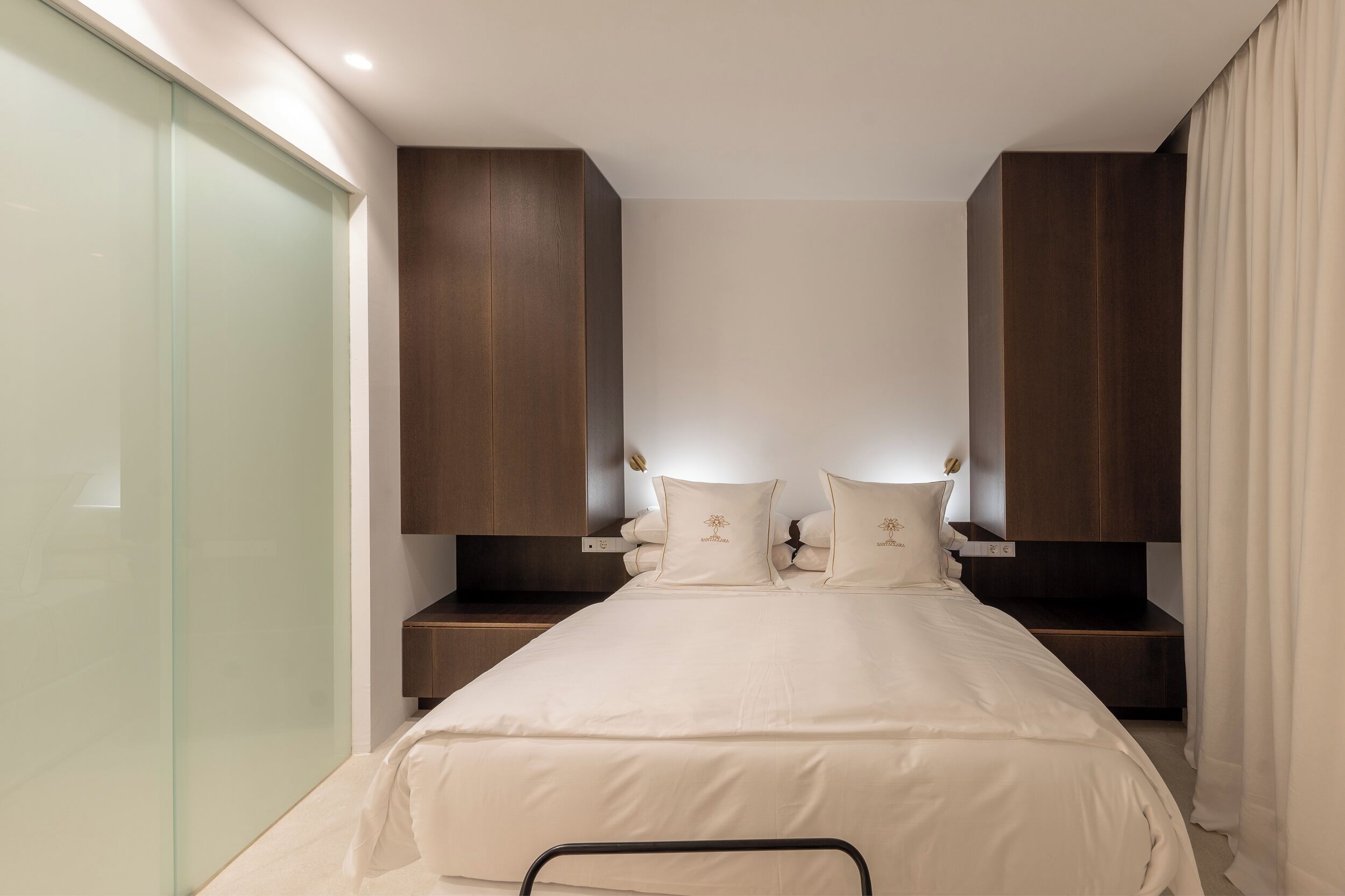 A bedroom with a bed centered between two wooden cabinets, a bedside table, and a glass door.