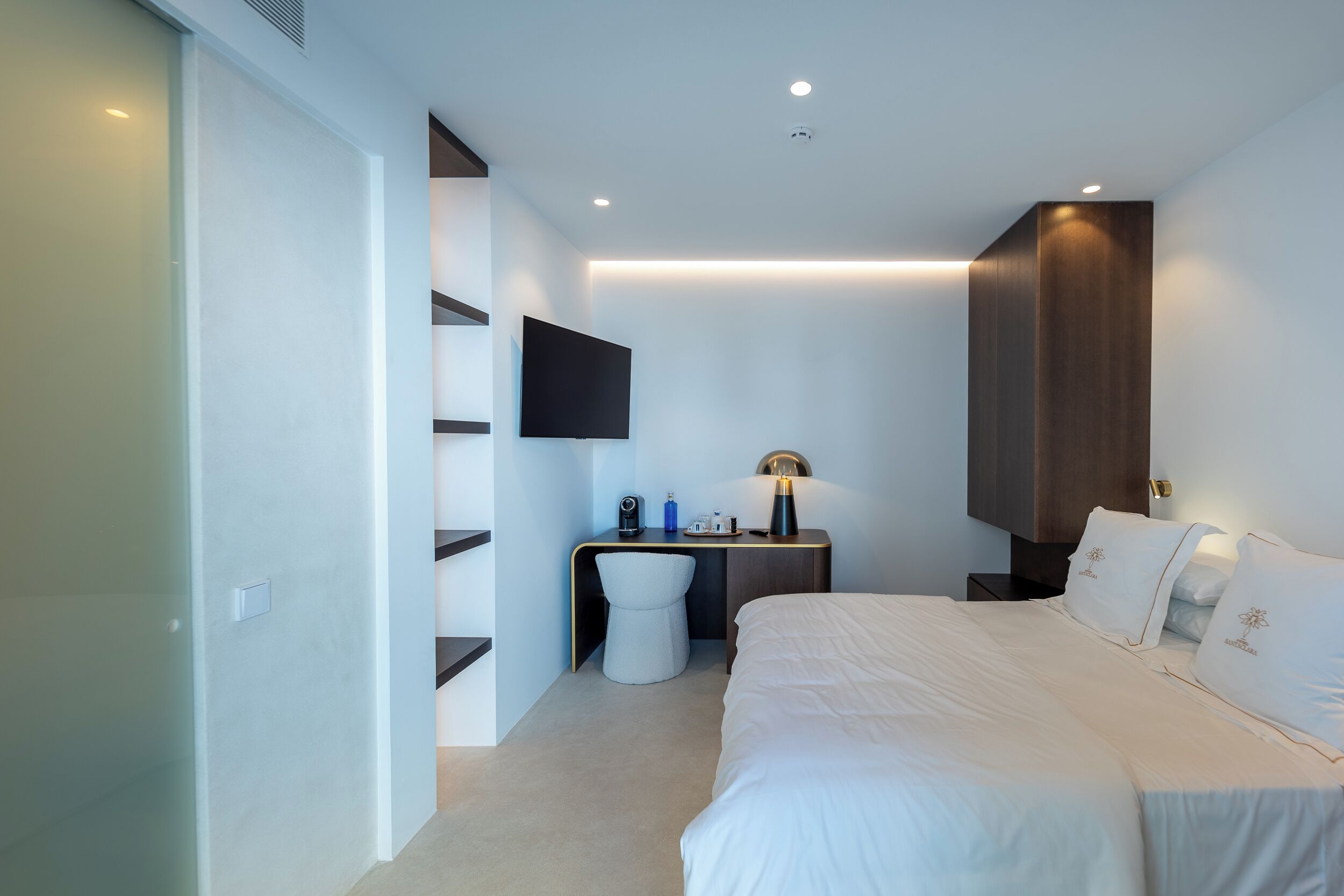 Une chambre d’hôtel moderne dotée d’un grand lit, d’un bureau avec une chaise, d’un téléviseur à écran plat fixé au mur et d’une table de chevet avec une lampe.