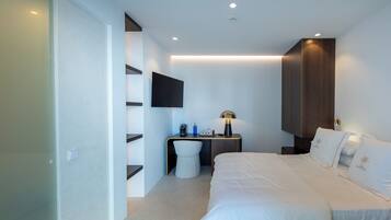 Une chambre d’hôtel moderne dotée d’un grand lit, d’un bureau avec une chaise, d’un téléviseur à écran plat fixé au mur et d’une table de chevet avec une lampe.