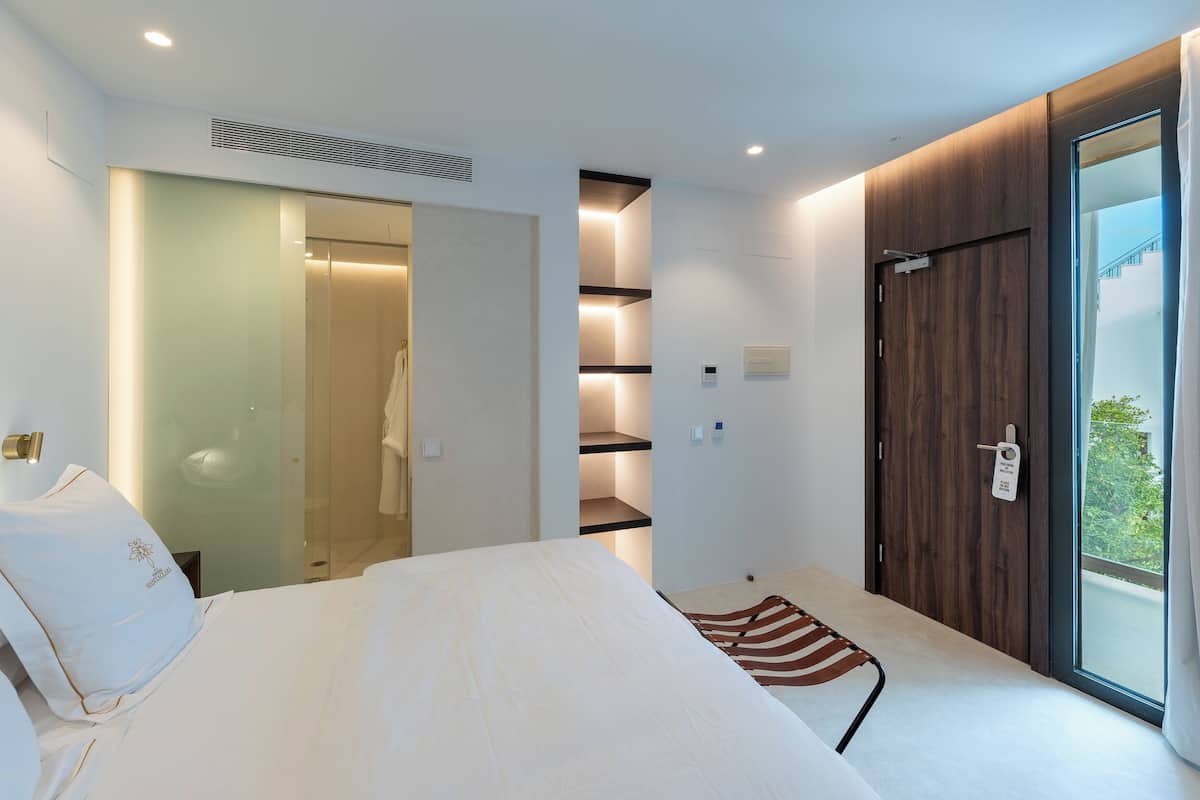 Une chambre d’hôtel moderne dotée d’un lit, d’un dressing et d’une grande fenêtre offrant une vue dégagée.