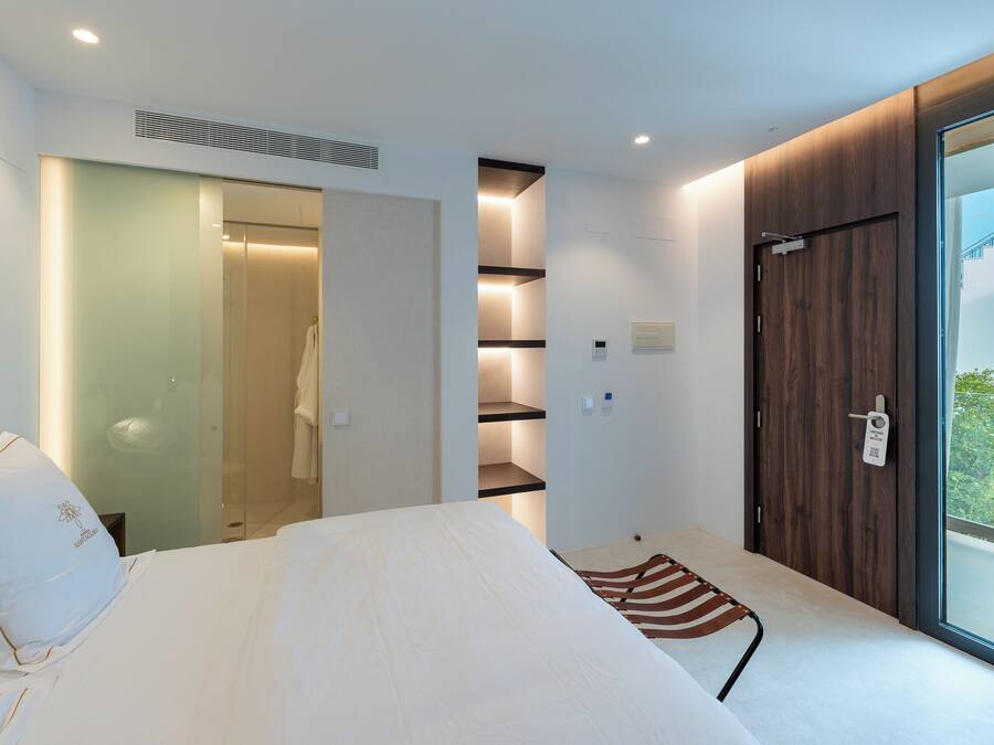 A modern hotel room with a bed, a walk-in closet, and a large window with a view.