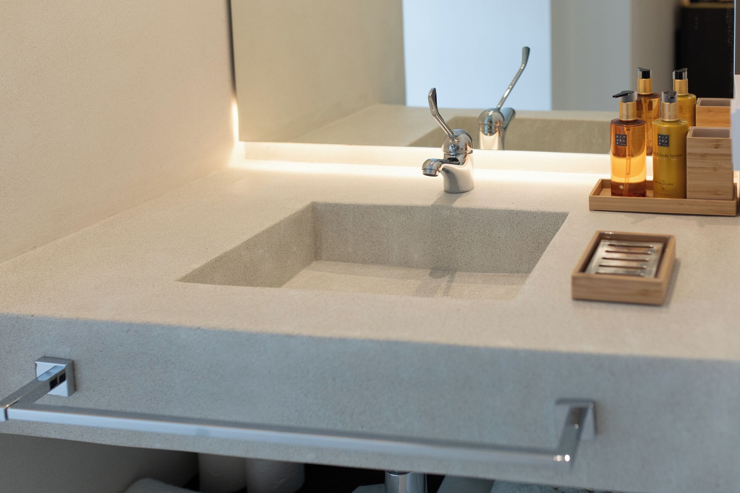 A modern bathroom with a large sink, a mirror, and a wooden tray holding toiletries.