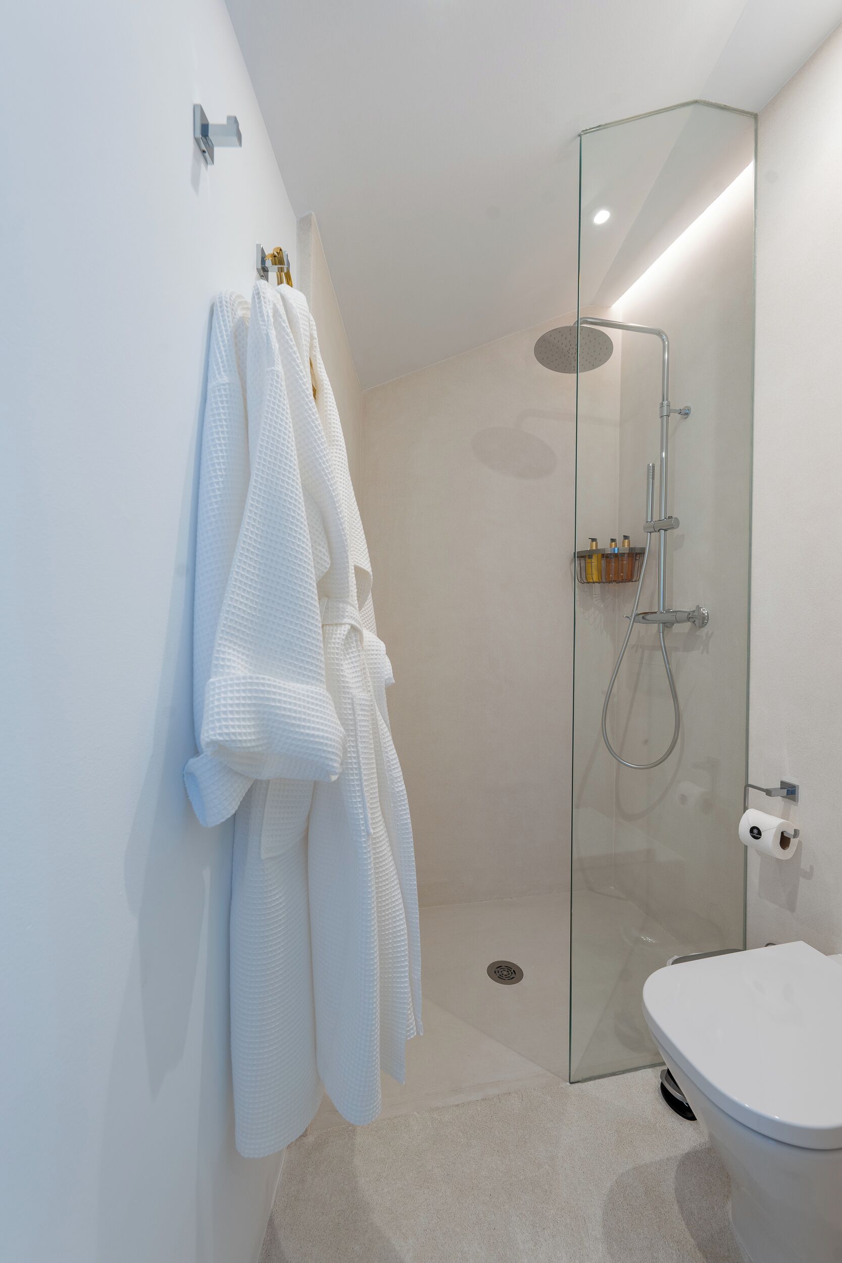 Un baño moderno con ducha de vidrio, inodoro y toallero con varias toallas.