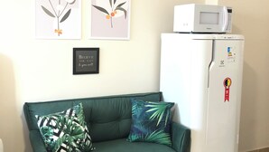 A room with a green sofa, two wall-mounted pictures, a framed motivational quote, and a white refrigerator with a microwave on top.