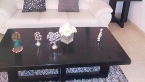 A living room with a white sofa, two pillows, a black coffee table with decorative items, and a small side table with a vase and a figurine.