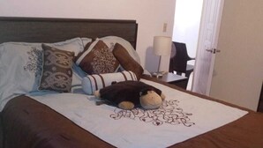 A neatly made bed with a brown bedspread, multiple pillows, and a teddy bear.