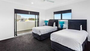 Habitación de hotel con dos camas, ventilador de techo y vistas de la ciudad a través de amplias ventanas.