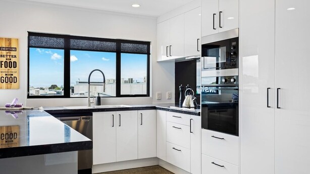 Una cocina moderna con armarios blancos, encimera negra y ventana con vista a la ciudad.