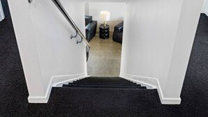 Una escalera conduce a una sala de estar con una lámpara y dos otomanes negros.