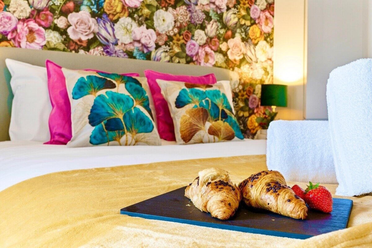 A bed with floral pillows, a blue tray with croissants and a strawberry, and a white towel.