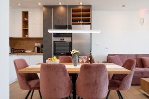 A modern kitchen with a built-in oven and microwave, a dining table with pink chairs, and a wooden countertop. - Exquisite and Stylish Apartment Trogir (Trogir)
