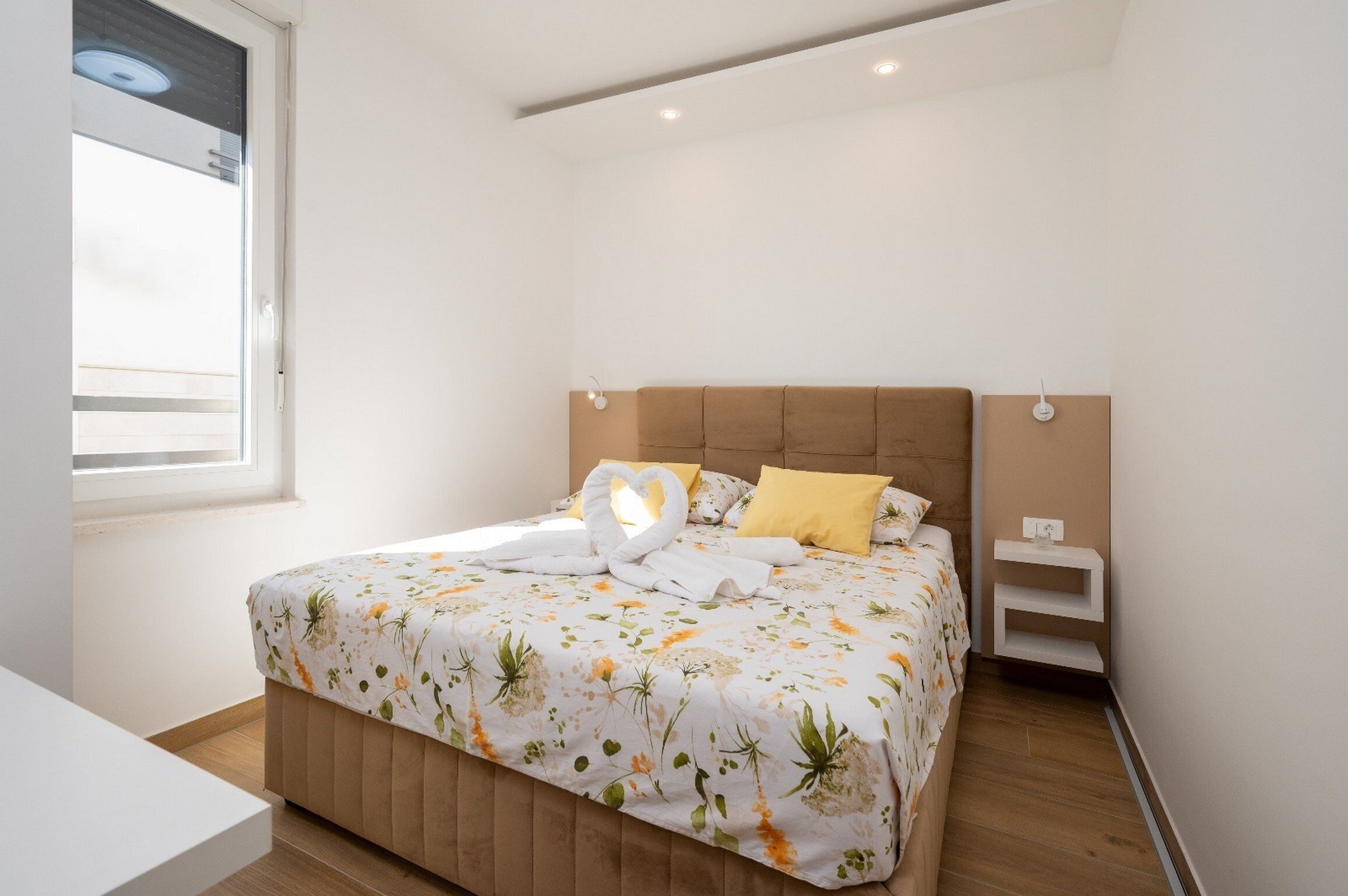Un letto rifatto con lenzuola a motivi floreali, un comodino e un tavolino di sostegno.