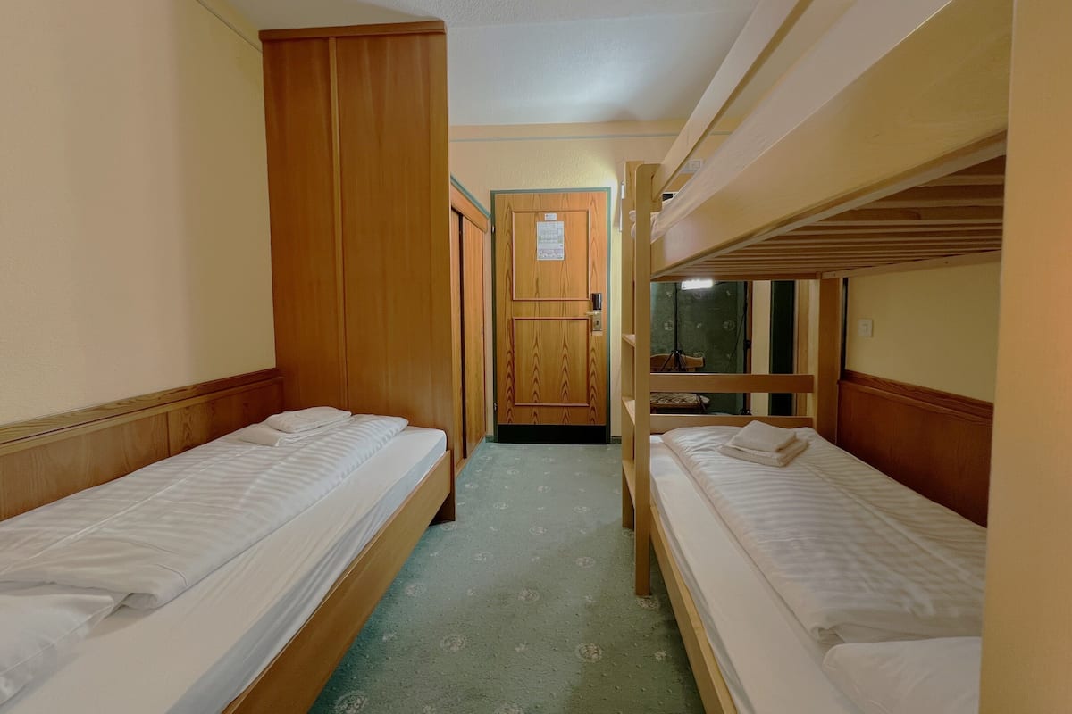 A narrow corridor with bunk beds on either side, wooden wardrobes, and a door at the end.